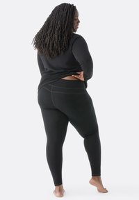 Schwarzes Sportoberteil und Leggings. Das Oberteil hat einen abgerundeten Saum, während die Leggings einen hohen Bund und dezente Nahtdetails aufweisen.