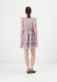 Lavendel, lager-på-lager klänning med volangärmar och elastisk midja. Har en flödande silhuett och lagerdelslängd, kombinerad med svarta slingbacks.