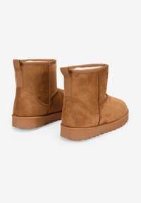 Stivaletti alla caviglia in suede marrone con un morbido rivestimento interno, punta arrotondata e suola in gomma texturizzata. Presentano delle linguette per una facile calzata.