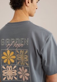 Gray cotton T-shirt with a relaxed fit, featuring a floral print in yellow, pink, and brown on the back, and text reading "GARDEN of hope."