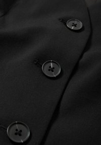 Gros plan sur un tissu noir avec trois boutons foncés cousus en ligne verticale sur un vêtement.