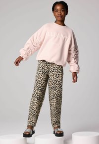 Sudadera de color rosa claro con mangas texturizadas, que presenta la letra "ALLSAINTS LONDON". Pantalones de leopardo beige. Sandalias de plataforma negras.
