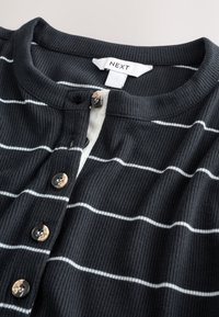 Haut noir en maille côtelée avec des rayures horizontales blanches, doté d'un col henley, de quatre boutons et d'une étiquette portant la mention "NEXT".
