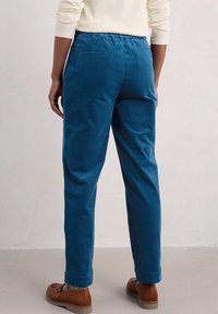 Pantaloni in velluto a coste blu con vestibilità rilassata, vita elastica e tasche laterali. Il modello indossa scarpe marroni, in piedi su uno sfondo neutro.