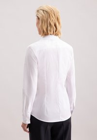 Biała koszula z długim rękawem o dopasowanym kroju, z tylnym szwem barkowym i mankietami zapinanymi na guziki, wykonana z gładkiego, lekkiego materiału.