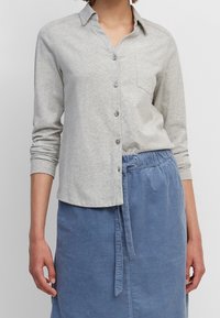 Light gray button-up shirt with a collar, long sleeves, and a chest pocket, paired with a blue corduroy skirt with a drawstring waist.