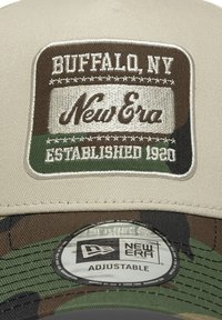 Căciulă de baseball bej cu interior camuflat. Prezintă un patch brodat cu textul "Buffalo, NY", "New Era" și "Înființată în 1920". Curea ajustabilă.