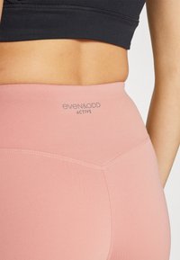 Roze tajice visoki struk s glatkom teksturom, s logotipom branda "even&odd ACTIVE" u sivoj boji blizu struka i šivanim detaljima.