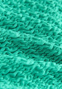 Eri tekstuuriga kangas erksa türkiissinise värviga, millel on lainekujuline kudumismuster. Pehme materjal nähtavate õmbluste ja siledaga viimistlusega.