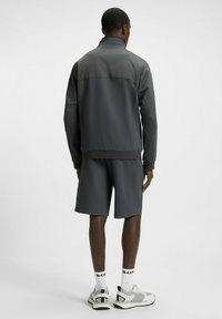 Grijze sportjack met hoge kraag, bijpassende shorts en grijze sneakers met zwarte accenten. Gladde stofstructuur met een modern ontwerp.