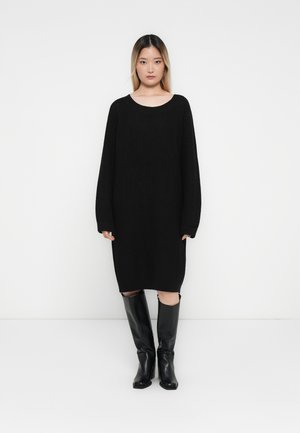 Black knitted dress with a wide neckline and long sleeves, featuring a loose fit and side slits. Paired with tall black leather boots.