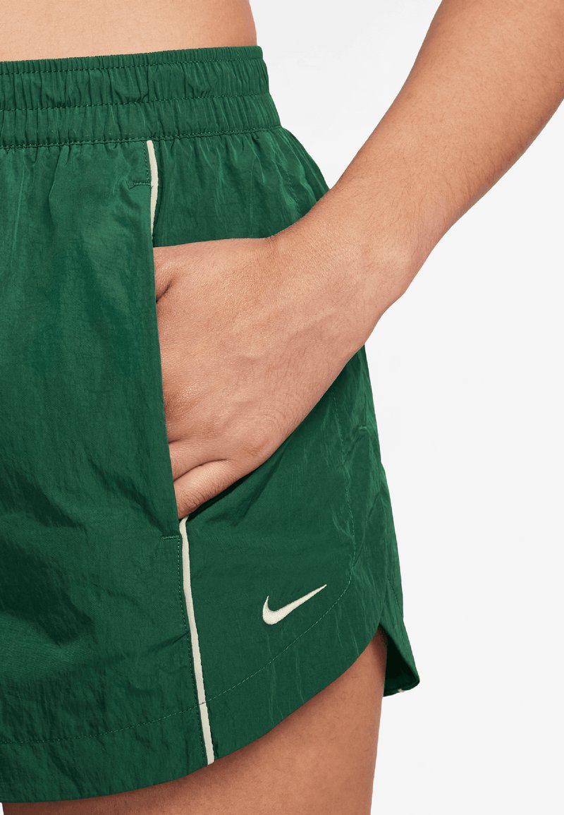 Shorts de sport verts en tissu texturé, avec une taille élastique, des poches latérales et un logo Nike blanc près de l'ourlet.