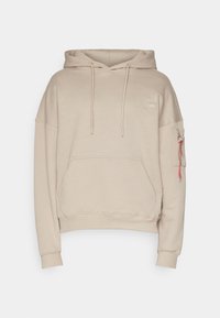Felpa beige con cappuccio realizzata in tessuto morbido. Presenta una tasca frontale, polsini a coste e una tasca laterale con zip e etichetta rossa.