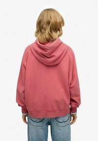 Sweatshirt rose à capuche avec une coupe décontractée, texture douce et poignets côtelés, associé à un jean en denim bleu clair.