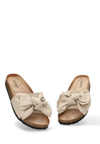 Las sandalias deslizantes de tela beige cuentan con un gran lazo en la correa, una plantilla suave similar al ante y una suela exterior de goma negra texturizada.