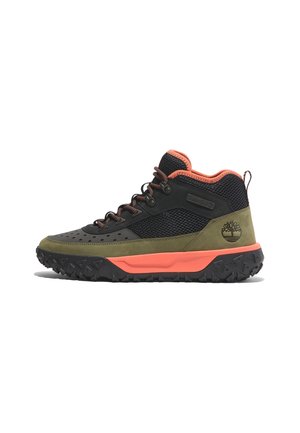 Chaussure outdoor mid-top en suède vert olive, mesh noir, accents orange, semelle noire robuste et logo Timberland au talon.