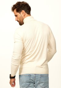 Cremefarbener Rollkragenpullover aus weichem Stoff, figurbetontes Design, gerippte Bündchen und Saum, kombiniert mit hellblauen Jeans, von hinten betrachtet.