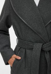 Sivi kaput od mješavine vune s pojasom u struku, velikim ovratnikom i kožnim detaljima. Ima bočne džepove i teksturiranu površinu.