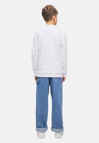 Vit långärmad skjorta och ljusblå vida jeans. Skjortan har en rundad halsringning; jeansen har sidofickor och uppvikta fållar.