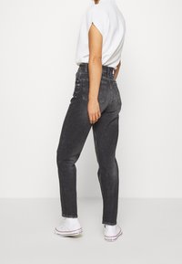 Höga svarta denimjeans med en avslappnad passform, med fem fickor och subtila blekningar, kombinerat med vita sneakers och en kortärmad topp.