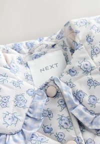 Gepolsterte Stoffjacke mit leichtem floralen Druck in Blau und Weiß. Merkmale sind ein geraffter Kragen, Knöpfe und ein "NEXT"-Label.
