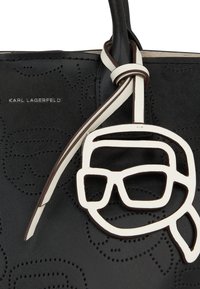 Bolso de cuero negro con un diseño perforado, acentuado con una etiqueta del logo de Karl Lagerfeld en blanco con forma de gafas y un detalle de cinta atada.