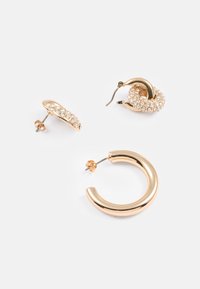 Sada náušníc v zlatohnedej farbe obsahujúca jeden pár hladkých kruhov a jeden pár so trblietavými kamienkami, ktoré predvádzajú rôzne tvary a textúry.