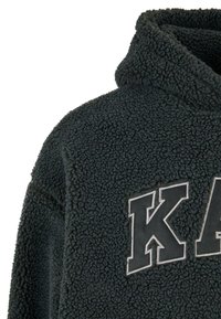 Tamno siva flis dukserica s visokom kragnom, teksturiranim materijalom i odvažnim "K" logotipom u svijetlosivoj koncu na prednjoj strani.