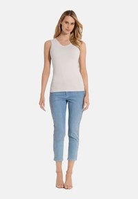 Lichtgrijze mouwloze top met een v-halsontwerp, gecombineerd met lichtblauwe jeans met versieringen aan de zijkant. Model draagt doorzichtige hakken.