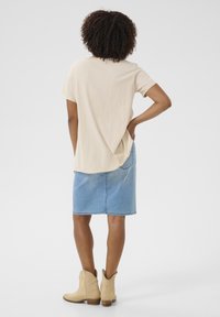 Béžové tričko s krátkým rukávem a zaobleným lemem, ve spojení s modrou džínsovou sukní. Nosí se s světle hnědými kotníkovými kovbojskými botami.