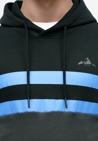 Hoodie preto com um padrão de riscas horizontais azuis, apresentando um capuz com cordões e um pequeno logótipo cinza de montanha no peito.