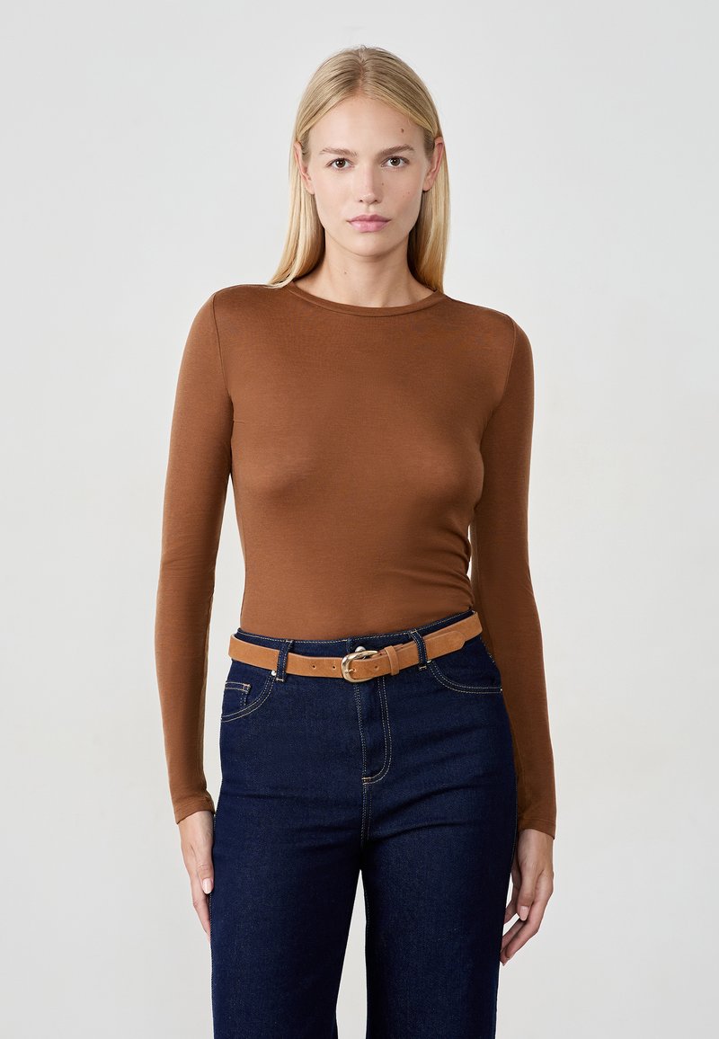 Braunes langärmliges Oberteil in taillierter Passform, kombiniert mit dunkelblauen High-Waist-Jeans und einem hellbraunen Gürtel mit einer runden Schnalle.