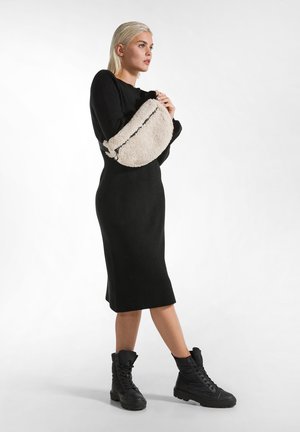 Sort ribbet kjole, knælængde med tætsiddende silhuet. Modellen holder en cremet faux fur taske med lynlås. Sorte combat støvler med strukturerede såler.
