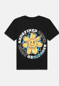 Zwarte T-shirt met een grote gele bloemafbeelding omringd door de tekst "REDEFINED REBEL" in wit met blauwe vlamaccenten.