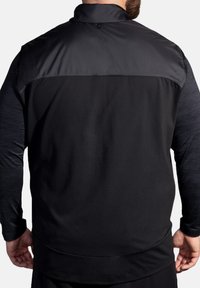 Schwarze Sportjacke mit glattem Oberteil und strukturierten unteren Ärmeln. Verfügt über einen hohen Kragen und ein schmal geschnittenes Design.