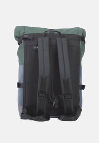 Rulltopryggsäck med en blandning av gröna, svarta och grå material. Utrustad med vadderade axelremmar och slitstark hårdvara. Strukturerade ytdetaljer.