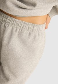 Jasnoszare dresy z elastycznym pasem i miękką teksturą, charakteryzujące się luźnym krojem i brakiem widocznych kieszeni. Projekt podkreśla komfort.