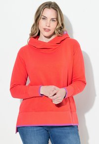 Sudadera roja con capucha tipo cowl, que cuenta con detalles en púrpura en las mangas y el dobladillo. Textura suave y corte relajado.