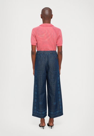 Polo shirt a righe rosse e bianche con maniche corte abbinato a pantaloni in denim scuro a gamba larga con una bordatura decorata lungo i lati.
