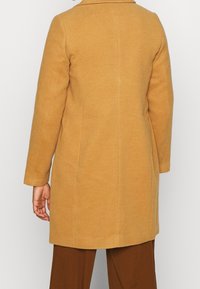 Manteau en laine beige clair avec une coupe droite, un col à revers et des manches longues. Présente une texture lisse et des coutures latérales.