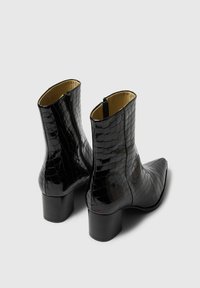 Melns lakots ādas potītes zābaks ar krokodila tekstūru, norādītu purngalu un vidēja augstuma bloku papēdi, ar sānu rāvējslēdzēju.