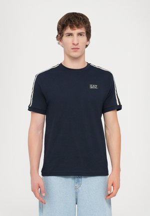 Navy blue T-shirt with rolled sleeves, featuring white side stripes and a small EA7 logo patch on the chest. Casual fit and smooth texture.