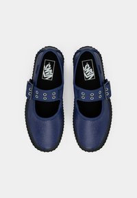 Een paar marineblauwe Vans Mary Jane schoenen met zwarte zolen en gespbanden liggen plat op een witte achtergrond.