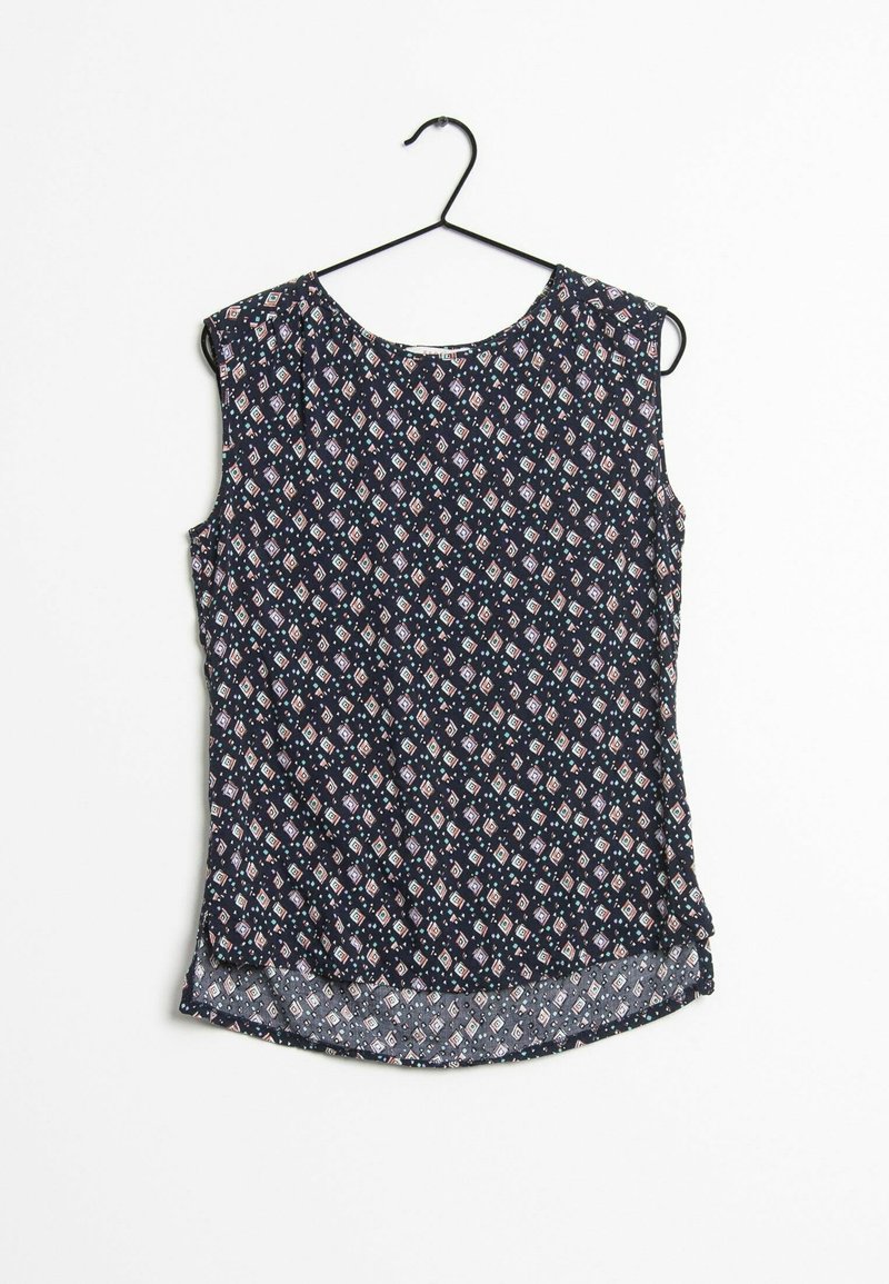 Blouse bleu foncé sans manches avec petits motifs géométriques blancs et roses en forme de losange, suspendue à un cintre noir sur un fond blanc.