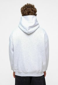 Grijze hoodie met een grote achterkant, verlaagde schouders en ribbelmanchetten. Zachte textuur; minimalistisch ontwerp zonder zichtbare logo's of accenten.