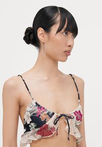 Blumiges Bikini-Oberteil mit Rüschendesign, das einen marineblauen Grundton und mehrfarbige Blumen aufweist. Verstellbare Träger und ein Schleifchen in der Mitte.