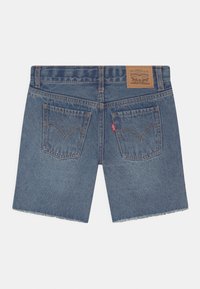 Jeansshorts i medelblått med fransar i nederkant; har två bakfickor med sömnadsdetaljer och ett brunt lädermärke på midjan.