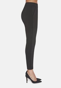 Czarne tapered pants wykonane z gładkiego materiału, z średnim stanem i subtelnymi fałdami z przodu, stylizowane z czarnymi, spiczastymi obcasami.