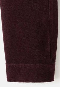 Pantalón de pana burdeos con una superficie texturizada, dobladillo limpio y detalle en la costura lateral, que refleja un acabado de tela suave.