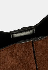 Braune Wildleder-Handtasche mit einem schwarzen Lederinnenraum. Sie verfügt über ein strukturiertes Design und sichtbare Nähte entlang der Kanten.